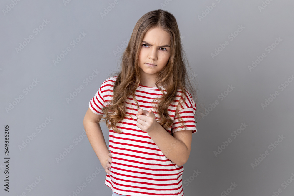 Portrait of little girl wearing striped T-shirt pointing finger at camera and looking with dissatisfied suspicious expression, warning about troubles. Indoor studio shot isolated on gray background. Portrait of little girl wearing striped T-shirt pointing finger at camera and looking with dissatisfied suspicious expression, warning about troubles. Indoor studio shot isolated on gray background.