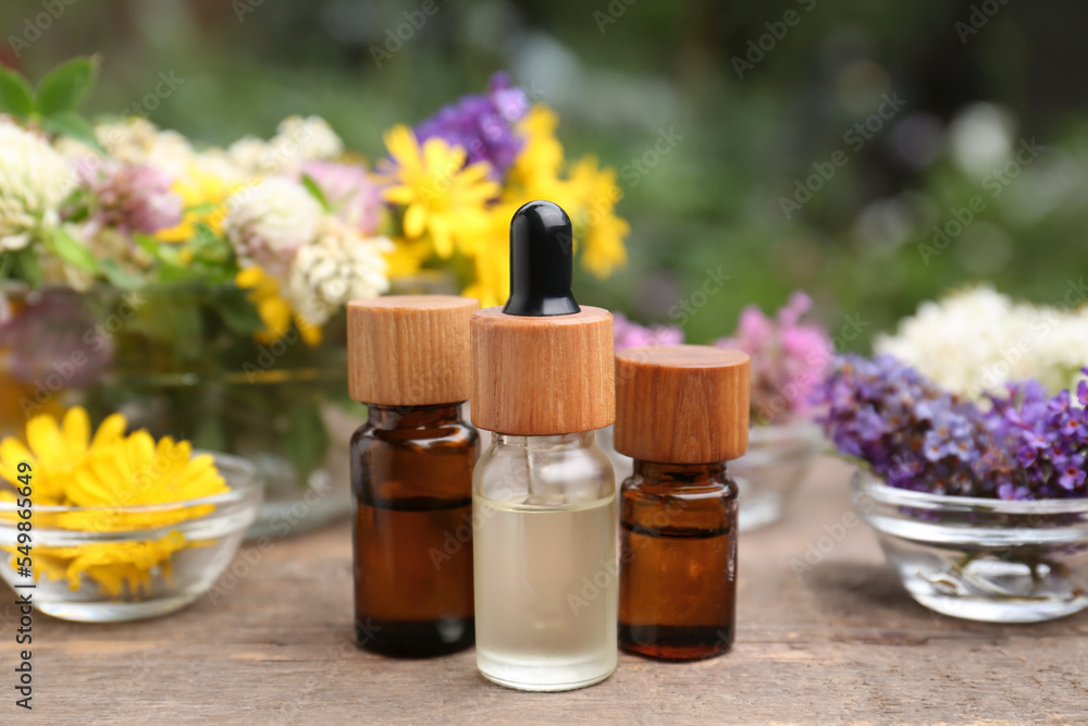 Bottles of essential oils and many beautiful flowers on wooden table Bottles of essential oils and many beautiful flowers on wooden table