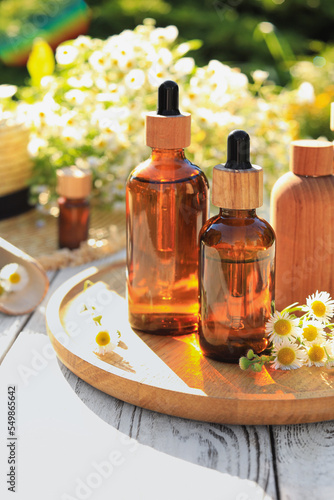 Bottles of essential oil and flowers on white wooden table outdoors