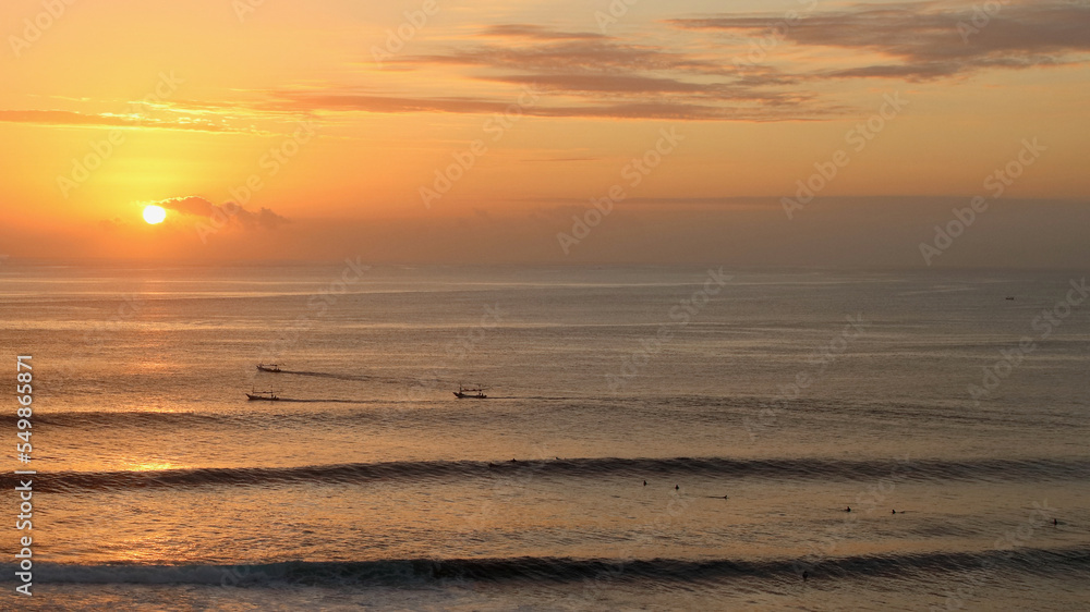 Amazing sunset at Uluwatu beach, where surfers and fishermen meet in the sea on dusk, Uluwatu, Bali, Indonesia.