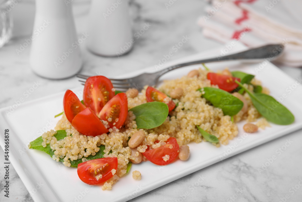 Delicious quinoa salad with tomatoes, beans and spinach leaves served on white marble table Delicious quinoa salad with tomatoes, beans and spinach leaves served on white marble table