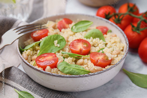 Delicious quinoa salad with tomatoes, beans and spinach leaves served on white marble table, closeup