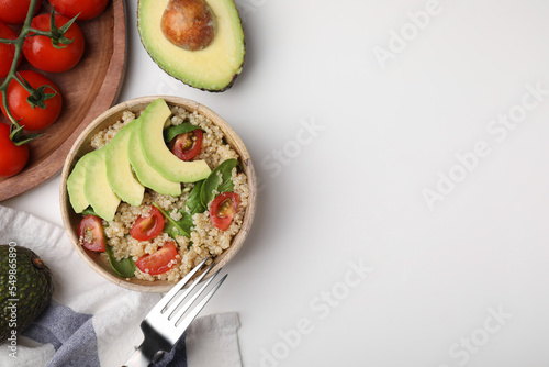 Delicious quinoa salad with tomatoes, avocado slices and spinach leaves served on white table, flat lay. Space for text