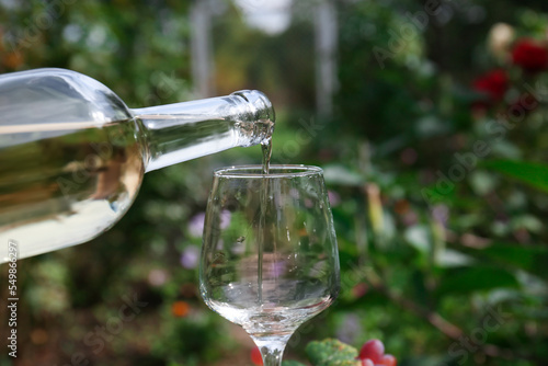 Pouring white wine from bottle into glass outdoors, closeup