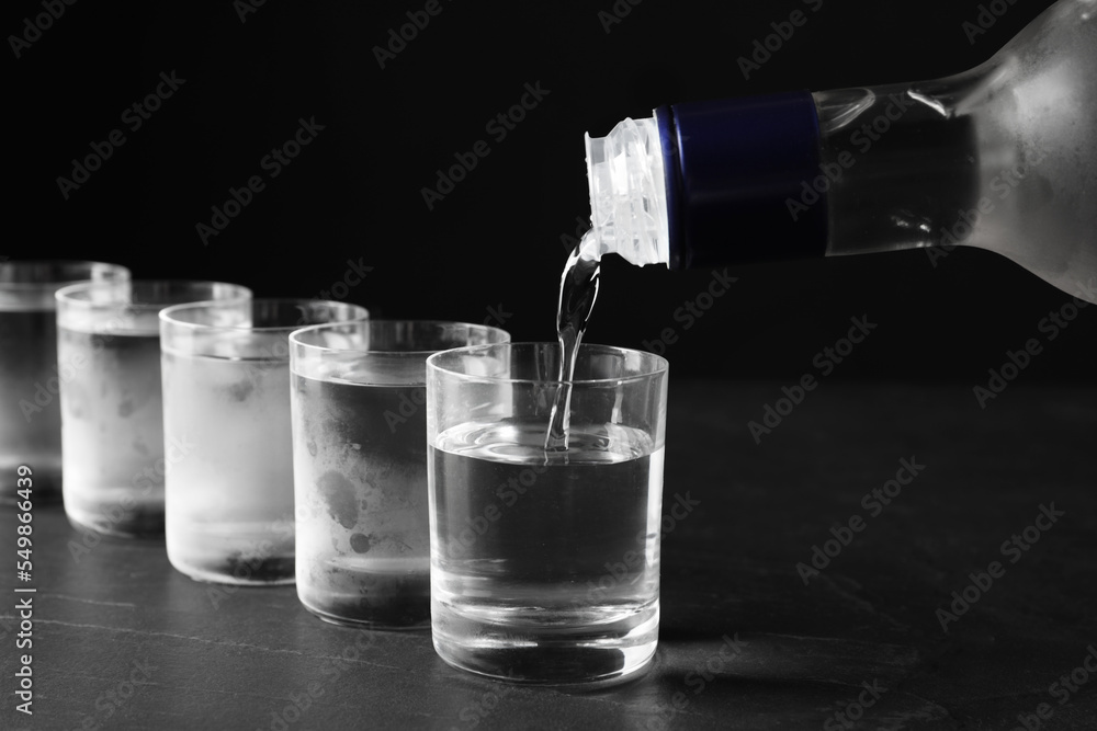 Pouring vodka from bottle in glass on grey table, closeup Pouring vodka from bottle in glass on grey table, closeup
