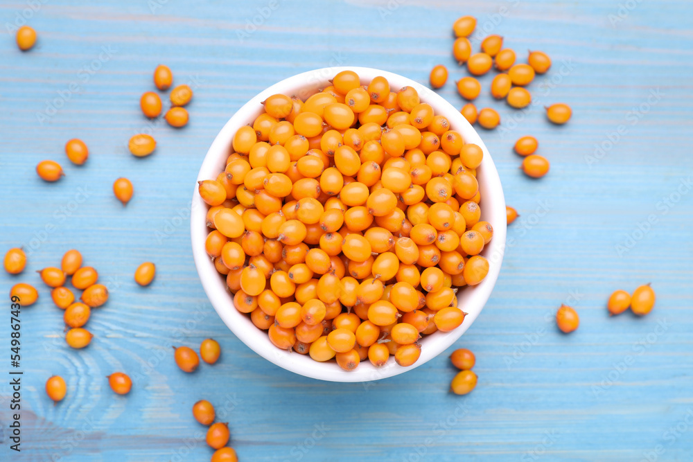 Bowl with fresh ripe sea buckthorn berries on light blue wooden table, flat lay Bowl with fresh ripe sea buckthorn berries on light blue wooden table, flat lay