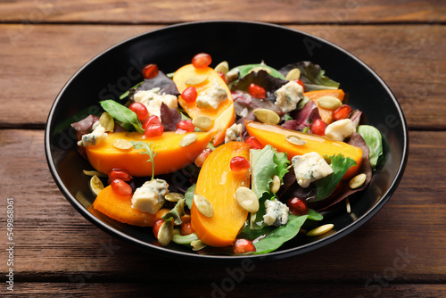 Delicious persimmon salad with pomegranate and spinach on wooden table