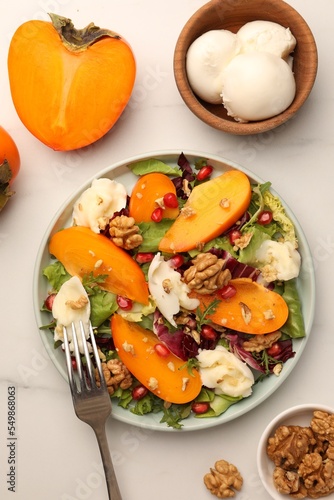 Delicious persimmon salad with cheese and pomegranate served on white table, flat lay