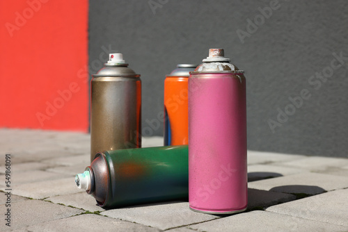 Cans of different spray paints on pavement near wall, closeup