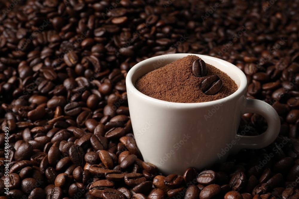Fototapeta premium Cup with ground coffee on roasted beans. Space for text