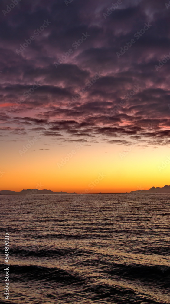 Naklejka premium Popcorn clouds illuminated pink over the silhouette of a mountain, at sunset at Cierva Cove, Antarctica