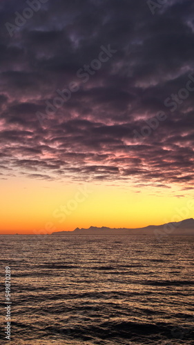 Popcorn clouds illuminated pink over the silhouette of a mountain, at sunset at Cierva Cove, Antarctica