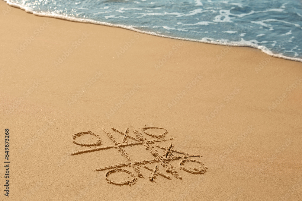 Tic tac toe game drawn on sand near sea, space for text Tic tac toe game drawn on sand near sea, space for text