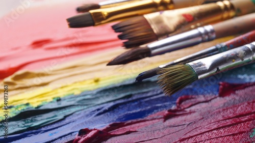 Many brushes on artist's palette with colorful mixed paints, closeup