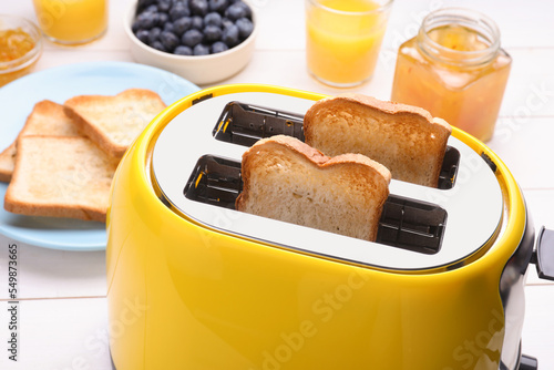 Yellow toaster with roasted bread, glasses of juice, blueberries and jam on white wooden table, closeup