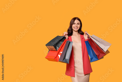 Beautiful young woman with paper shopping bags on yellow background. Space for text