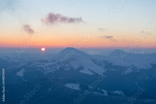 The sun disk rises above a snow-covered mountain at dawn. Petros and Hoverla Peaks