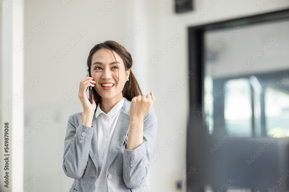 Young smiling Happy excited Business asian woman talking on mobile phone, standing in workplace office with document in her hand Young smiling Happy excited Business asian woman talking on mobile phone, standing in workplace office with document in her hand