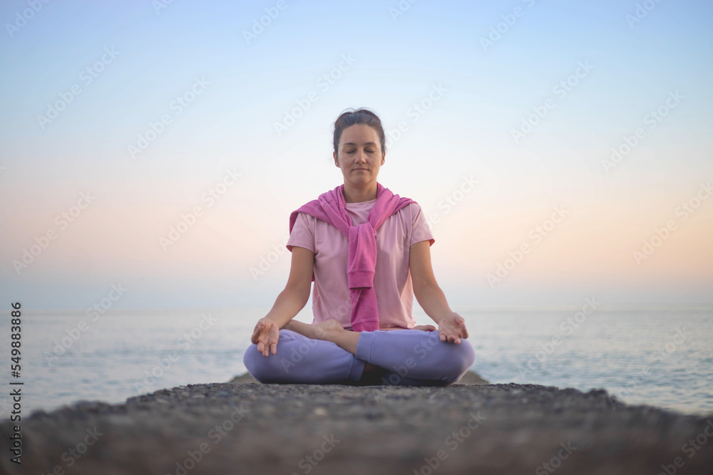 Yoga woman meditation in lotus position at pebble sea beach sunset sky horizon healthy lifestyle