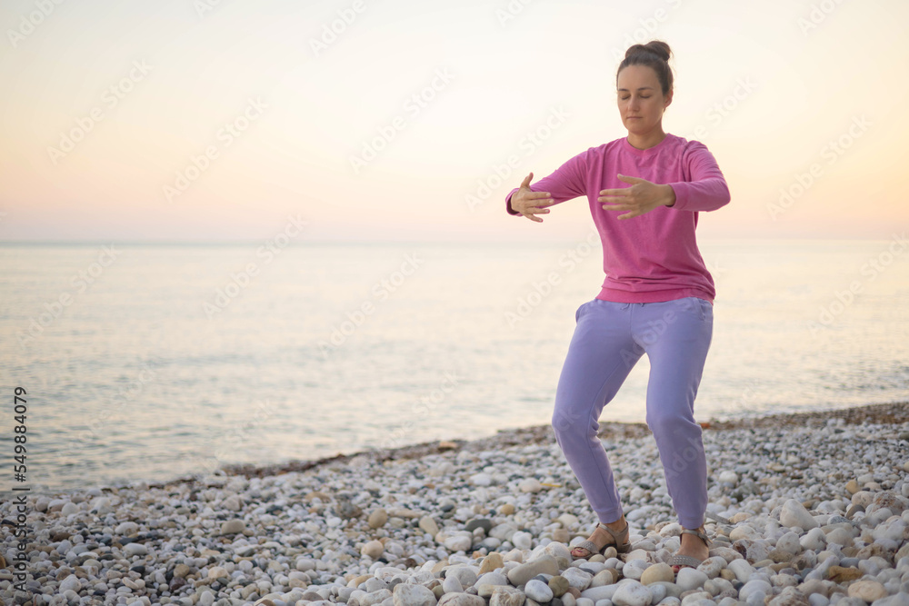 Yogi woman practicing zhangzhuang pillar work asana posture with closed eyes on pebble sunset beach