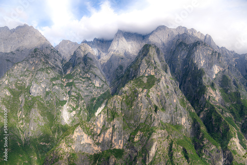 Beautiful panorama view of Jade Dragon snow mountain from hiking trail path of Tiger Leaping Gorge with blue sky in background, is located in Yulong Naxi autonomous in Lijiang city, Yunnan, China