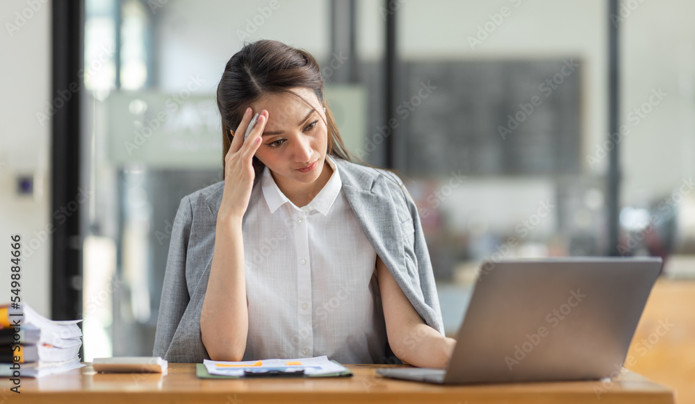 Portrait of tired young business Asian woman work with documents tax laptop computer in office. Sad, unhappy, Worried, Depression, or employee life stress concept Portrait of tired young business Asian woman work with documents tax laptop computer in office. Sad, unhappy, Worried, Depression, or employee life stress concept