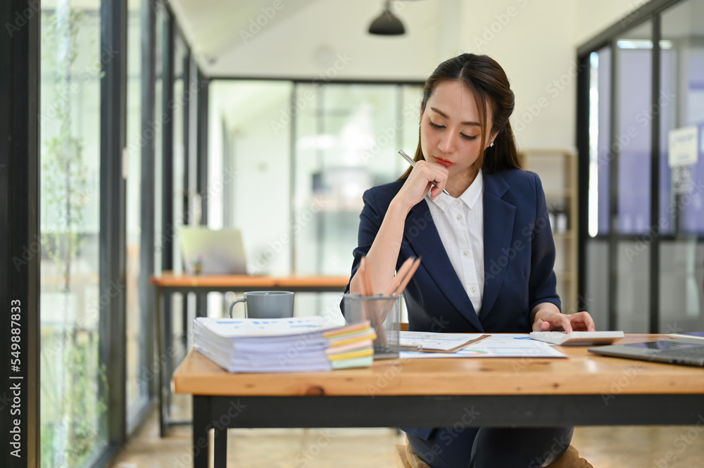 Professional businesswoman focusing on her tasks, analyzing sales report, working at her desk Professional businesswoman focusing on her tasks, analyzing sales report, working at her desk