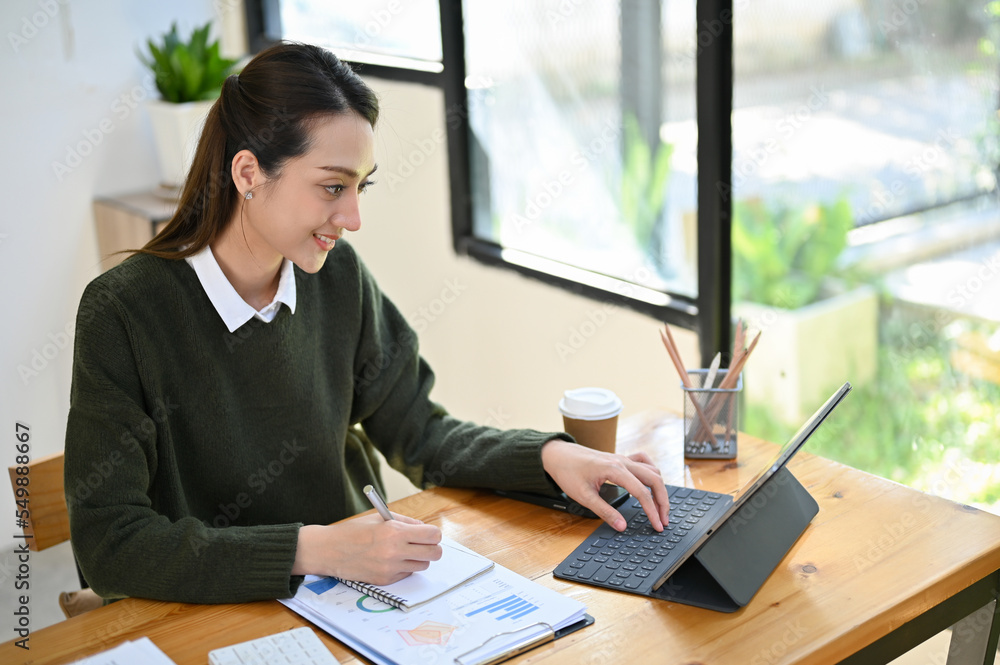 Beautiful Asian businesswoman focusing on her task, using tablet, working at her office desk. Beautiful Asian businesswoman focusing on her task, using tablet, working at her office desk.