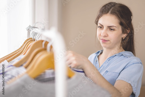 Young beautiful woman stands near the closet and hangs up her clothes. Clothes storage.