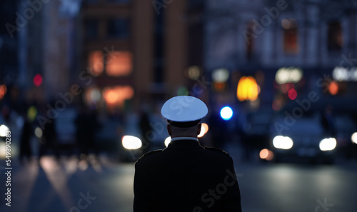 A military police soldier officer photographed from behind with car lights and silhouettes in background.