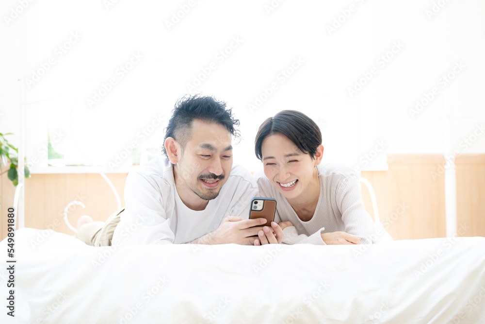 Fototapeta premium Image of an Asian couple lying down and looking for something on their phone. 