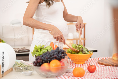young pregnant woman makes herself salad of fresh vegetables, the concept of proper nutrition. high quality photo. pregnant woman in kitchen making salad.