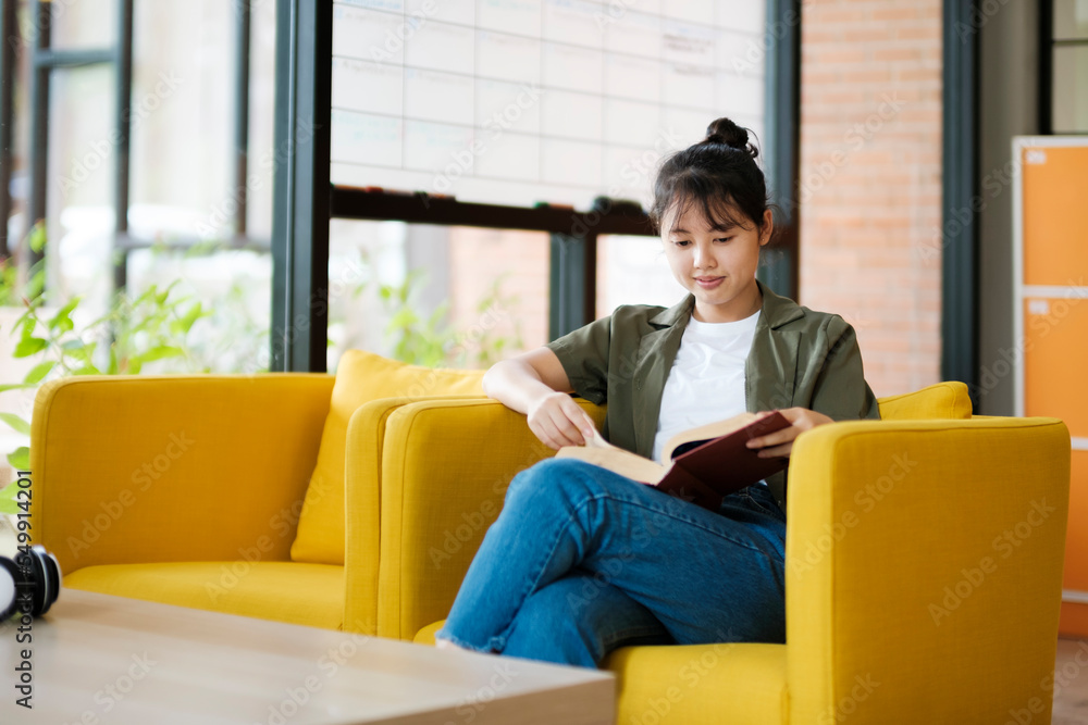 Young woman sitting indoors reading book while sitting on couch at home. Young woman sitting indoors reading book while sitting on couch at home.