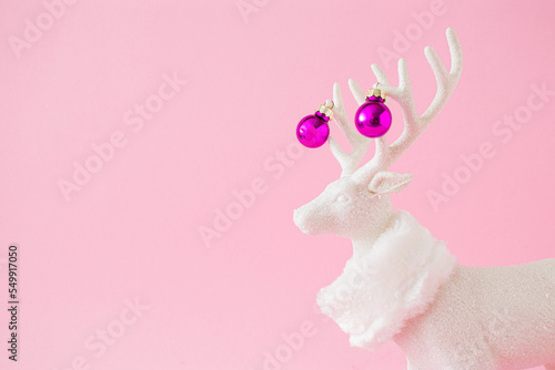 Fototapete White reindeer with scarf and pink Christmas baubles against a pastel pink background