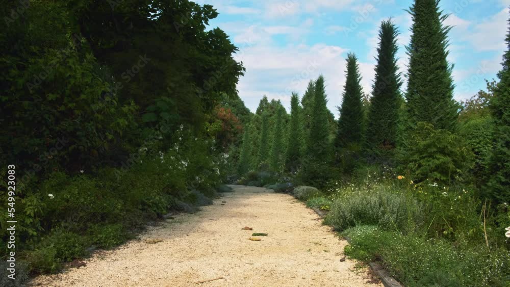 centered orange gravel european pathway turns the curve, left and right along the track surrounded by mediterranean green shrubs and plants, blue clean sky above filled with some summer clouds centered orange gravel european pathway turns the curve, left and right along the track surrounded by mediterranean green shrubs and plants, blue clean sky above filled with some summer clouds