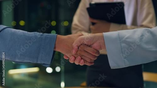 Closeup multiracial group of young creative people in smart casual wear discussing business shaking hand together while standing in modern night office. Partner cooperation, coworker teamwork concept. photo