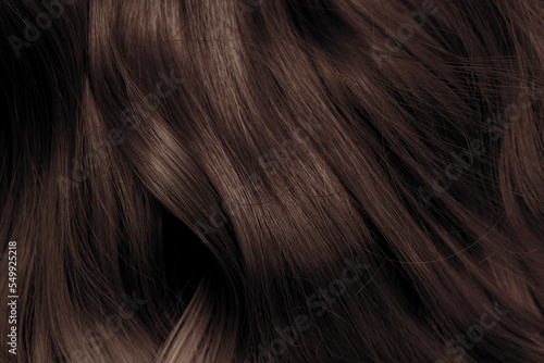 Brown hair close-up as a background. Women s long brown hair. Beautifully styled wavy shiny curls. Hair coloring. Hairdressing procedures  extension.