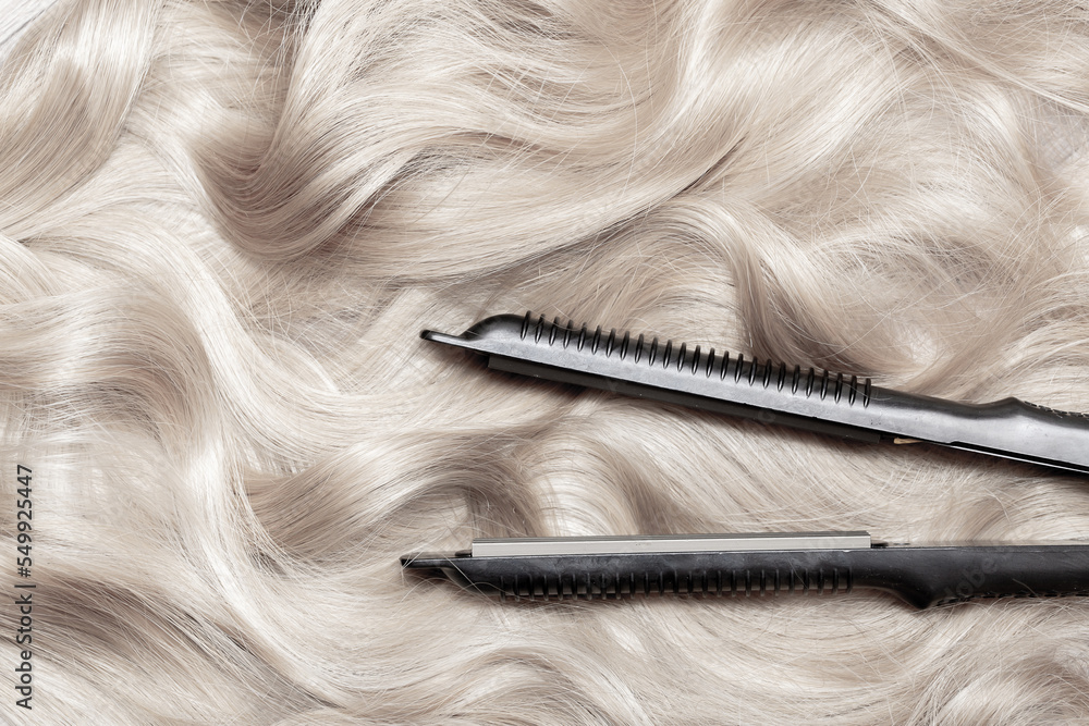 Naklejka premium Iron for straightening and styling hair in a beauty salon. Curling your hair into beautiful wavy curls with a hair straightener. Flat lay top view as background with place for text.