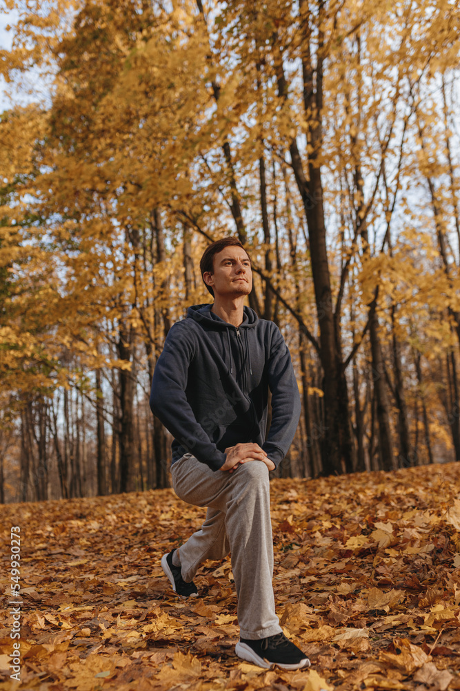 Confident male runner stretching legs and doing lunge exercise while training in park on sunny day in autumn Confident male runner stretching legs and doing lunge exercise while training in park on sunny day in autumn