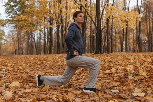 Side view full length of sportsman doing lunge exercise during fitness training in autumn park 