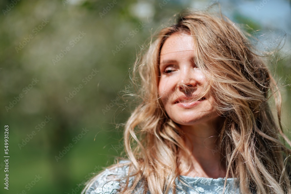 Naklejka premium Portrait of a blonde in the park. Beautiful woman with long blond hair in a blue dress.
