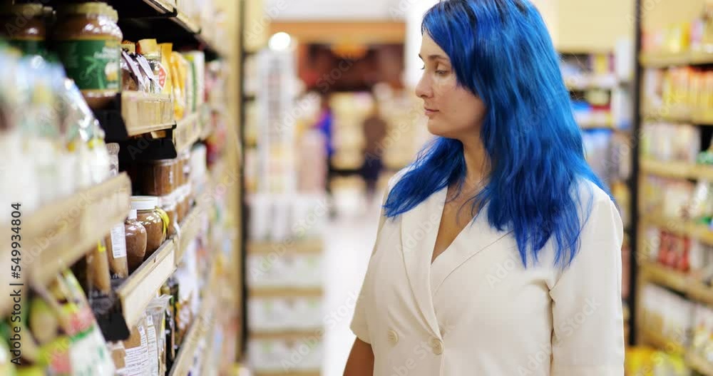 Housewife in grocery store, taking plastic jar of brown sugar from the shelf and comparing it with another one. Young woman choosing what to buy at supermarket, portrait shot with blurred background Housewife in grocery store, taking plastic jar of brown sugar from the shelf and comparing it with another one. Young woman choosing what to buy at supermarket, portrait shot with blurred background