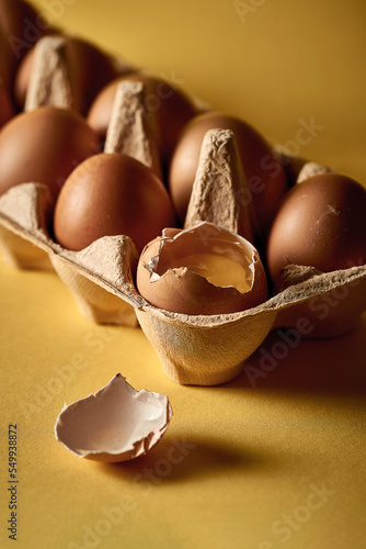 The poster concept is not like everyone else's. A broken egg in a cardboard package with other eggs. Yellow background, selective focus. Close-up photo