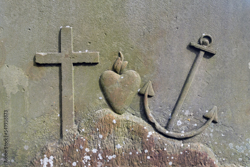 the religious symbols anchor, heart and cross carved in stone