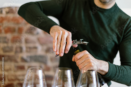 barman uncorks a bottle to fill glasses for wine tasting photo