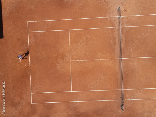 Aerial top view of a young female tennis player playing on brown ground court. Professional girl tennis player hitting a backhand on court Flat layout sport background.  © .shock