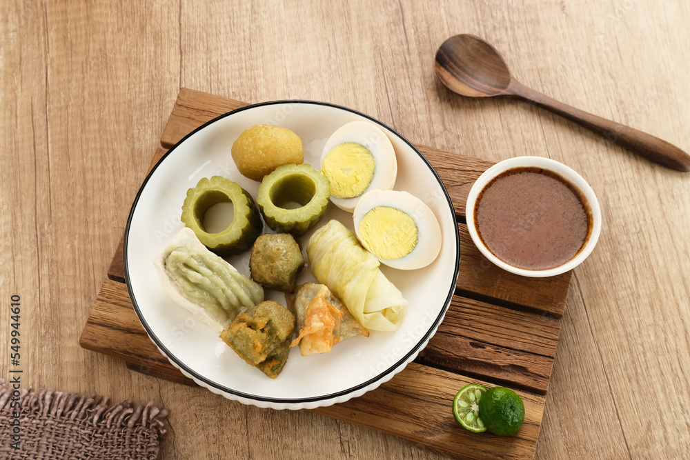Siomay Bandung (Shumay) or steamed dumplings with boiled egg, tofu, potatoes and cabbage roll. Indonesian traditional street food with peanut sauce and soy sauce, and green lime.
