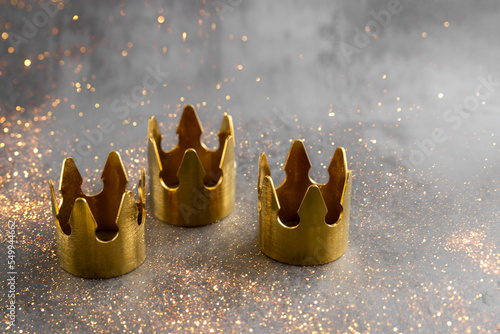 Epiphany  Day or Dia de Reyes Magos concept. Three gold crowns on black background with golden particles. photo