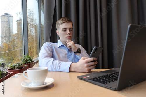 A young man works at a laptop at a table in the room. 