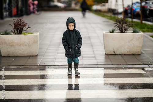 Photos A boy with hands in his pockets is crossing a street downtown on the rain